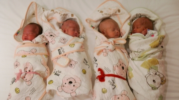 One-month-old quadruplets are swaddled in blankets at a hospital.