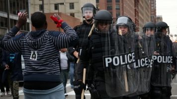 A protester holds up his hands as police in riot gear pass.