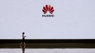 A member of Huawei's reception staff walks in front of a large screen displaying the logo.