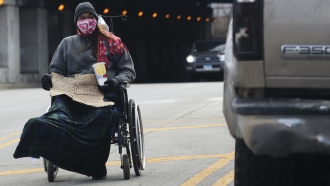 A homeless person carrying a sign and wearing a mask