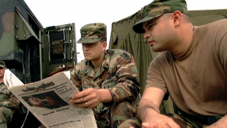 Two soldiers look in on a Stars and Stripes publication
