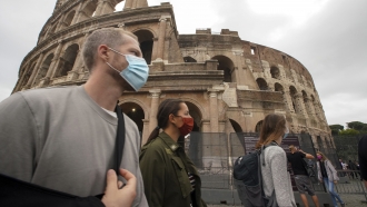 People wear face masks to prevent the spread of COVID-19 as they stroll by the ancient Colosseum, in Rome.