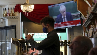 A member of staff pours a drink in a pub as the TV screen shows Prime Minister Boris Johnson delivering a statement.