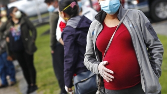 A pregnant woman wearing a face mask and gloves.