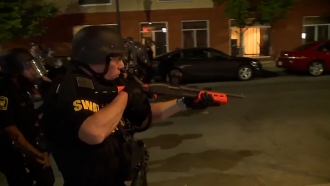 A SWAT officer points a shotgun at night while working the streets