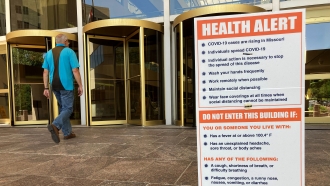 A sign warning of COVID-19 dangers remains in place outside a state office building in Jefferson City, MO.