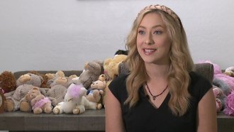 Woman sits in front of stuffed animals.