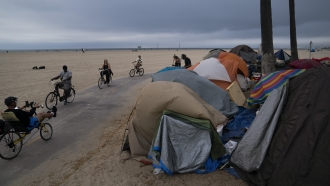 People ride bikes past a homeless encampment in Los Angeles, California.