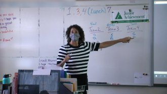 Teacher stands in front of a whiteboard.