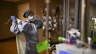 A nurse puts on a protective gown before entering the room of a COVID-19 patient