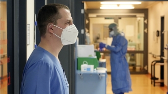 An ICU nurse stands in front of an isolation room.