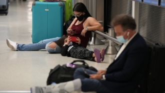 A woman and child wait for their flight alongside another traveler, at Miami International Airport
