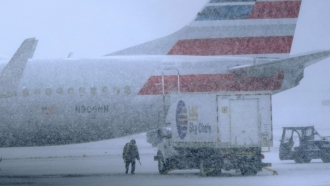 Snow falls as a ground crew works outside a parked plane