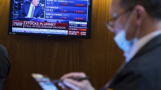 A man checks the markets as TV shows stocks after Ukraine invasion.