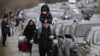 Ukrainian refugees walk along vehicles lining up to cross the border from Ukraine into Moldova