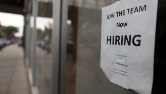 A "now hiring" sign hangs in the window of a Chinese restaurant