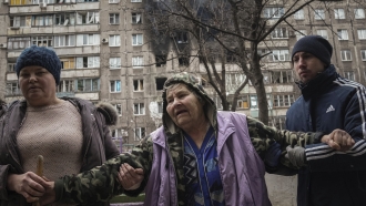 People help an elderly woman walk in Mariupol, Ukraine