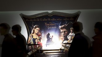 People walk past a "Beauty and the Beast" movie ad.