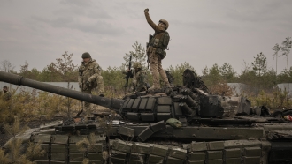 Ukrainian soldiers stand on top of a Russian tank