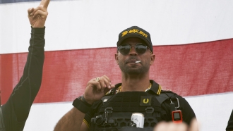 Proud Boys leader Enrique Tarrio wears a hat that says The War Boys and smokes a cigarette at a rally