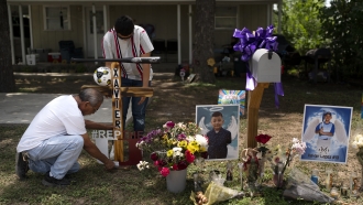Jose Mata, top, a brother of Xavier Lopez, and a man, who declined to give his name, place a wooden cross at a memorial