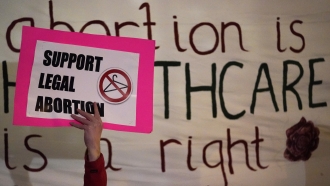 A sign saying "Support Legal Abortion" is shown.