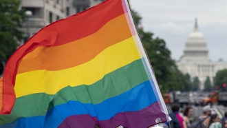 a person waves a rainbow flag as they participant in a rally in support of the LGBTQIA+ community