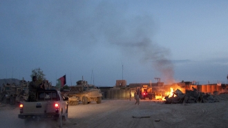 An Afghan National Army pickup truck passes parked U.S. armored military vehicles, as smoke rises from a fire