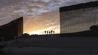 a pair of migrant families from Brazil pass through a gap in the border wall to reach the United States