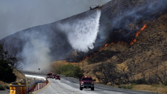 A helicopter drops water on the advancing Route Fire over emergency vehicles