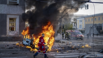 A medical worker moves past a burning car after a Russian attack in Kyiv, Ukraine.