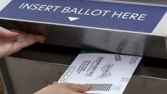 A voter inserts her absentee voter ballot into a drop box