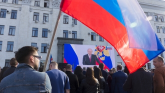 People with Russian national flags watch Russian President Vladimir Putin's address