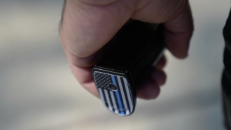 Bottom of gun in a man's hand shows an American flag decal with a blue line