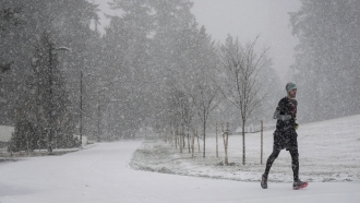 Heavy snow falls as a man jogs on a pathway at Central Park in Burnaby, British Columbia