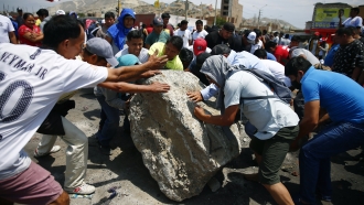 Supporters of ousted Peruvian President Pedro Castillo work together to roll a boulder onto the Pan-American North Highway.