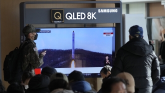 A TV screen shows a North Korean rocket launch.
