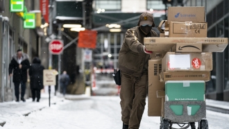 A UPS worker pushes cart of packages through snowfall.