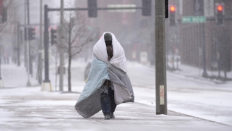 A person wrapped in a blanket walks on a sidewalk.