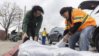 Two men collect sandbags from an emergency distribution center to prepare for an upcoming storm