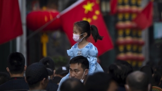 A girl wearing a face mask rides on a man's shoulders in Beijing, China