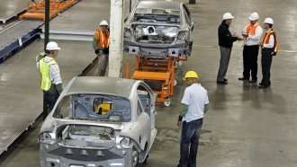 Workers stand near underbodies of cars.
