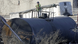 A cleanup worker stands on a derailed tank car.