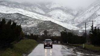 A motorist drives on a wet road under a snow-covered hillside