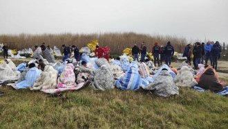 Rescued migrants sit covered in blankets at a beach near Cutro, southern Italy