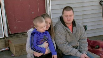 A couple and a child sit outside a home.