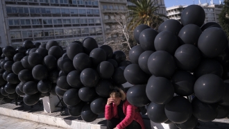 A woman sits among black balloons during a protest outside the Greek parliament in Athens.