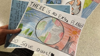 A person holds drawings and letters from elementary school students asking lawmakers to stop climate change