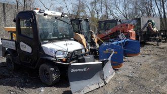 Snow plows sit in a dirt lot