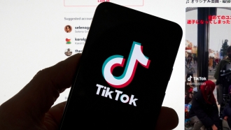 The TikTok logo is seen on a mobile phone in front of a computer screen